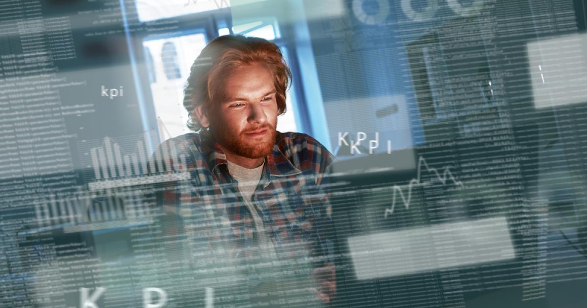 Foto de un hombre concentrado frente a una computadora con códigos al lado suyo