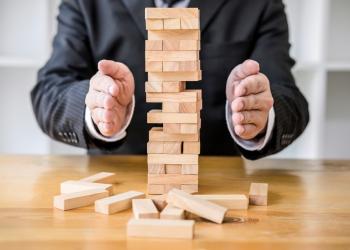 Persona tratando de que una torre hecha con bloques de madera no se caiga