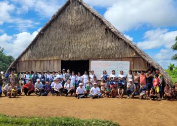Foto de una casa en paja con 30 personas al frente de ella posando para una fotografía