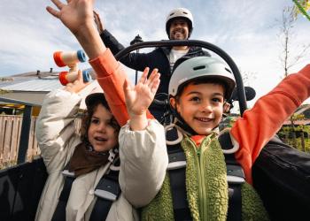 Foto de dos niños disfrutando en una montaña rusa, están alzando las manos