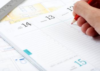 Foto de un calendario genérico con una mano encima y una persona escribiendo sobre él