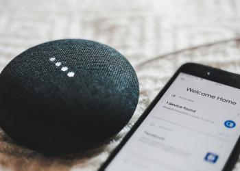 Foto de un celular y una alexa al costado, dispositivo electrónico