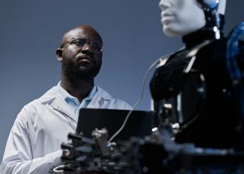 Foto de un hombre americano escribiendo sobre un teclado y mirando un robot