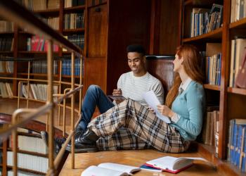 Foto de un hombre y una mujer sentados en una biblioteca leyendo unos libros