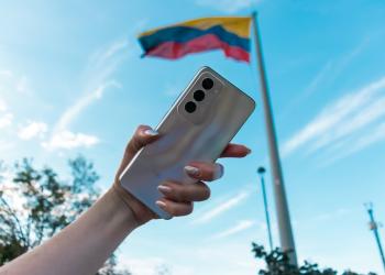 Foto de una mano de mujer con un celular y una bandera de fondo