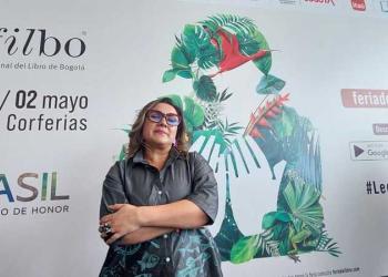 Foto de una mujer con gafas rofas mirando a la cámara, plano americano