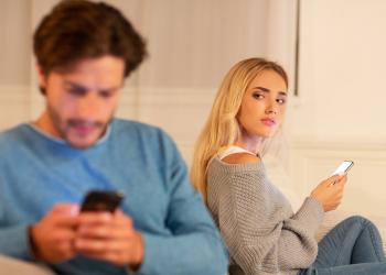 Foto de una mujer con un celular en la mano mirando de forma sospechosa a su pareja que habla por celular