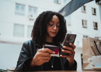 Foto de una mujer con un celular en la mano y una billetera en la otra