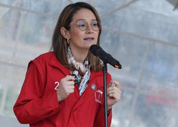 Foto de una mujer hablandole a un microfono con una chaqueta roja