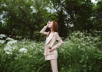 Foto de una mujer mirando hacía el cielo con un campo de flores en la espalda