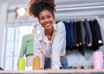 Foto de una mujer sonriendo a la cámara y de fondo unos vestidos