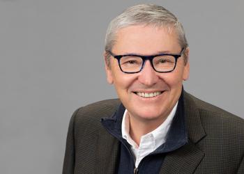 Foto de una persona adulta con gafas negras y canas mirando a la cámara