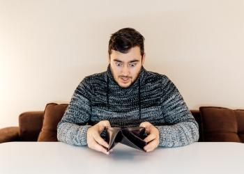 Foto de una persona jóven mirando consternado la billetera