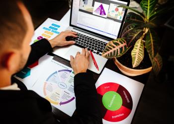 Foto de una persona mirando un computador y unas gráficas en una mesa