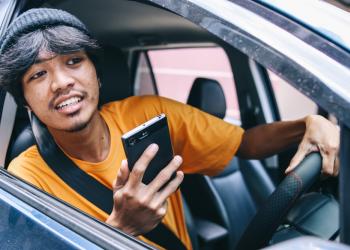 Foto de una persona sacando la cabeza por la ventana con un celular en la mano