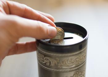 Foto de unos dedos ingresando unas monedas en la alcancia