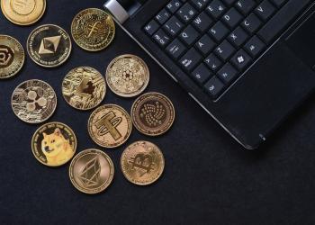 Foto de varias monedas cripto sobre una mesa con un computador al costado derecho