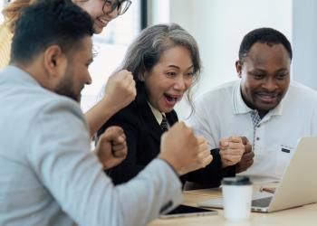 Foto de varias personas reunidas celebrando frente al computador