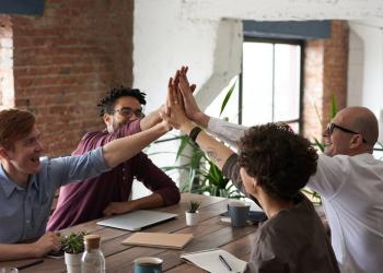 Fotografía de varias personas en el trabajo chocando manos sobre una mesa