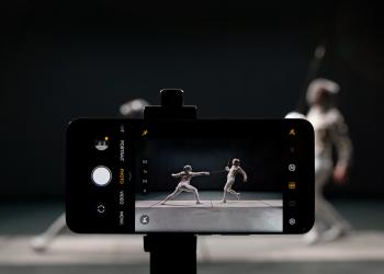 Foto de una celular tomando una foto de dos personas jugando esgrima con fondo negro