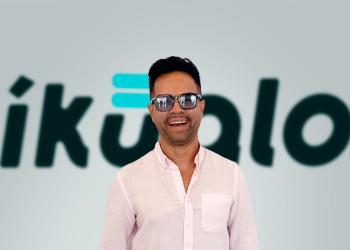 Fotografía de un hombre sonriendo con unas gafas y de fondo el nombre de Ikualo