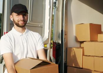 Foto de un un hombre con camiseta blanca y gorra negra alzando una caja sonriendo a la cámara