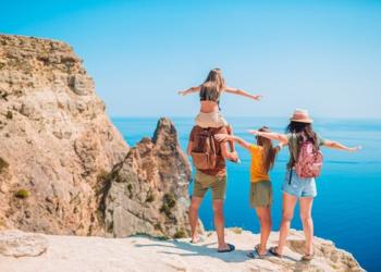 Imagen de una familia mirando al mar con un sol a sus espaldas
