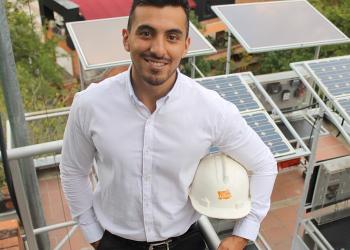 Foto de una persona con un casco posando frente a la cámara con unos paneles solares de fondo