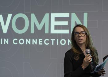 Mujer hablando en un escenario profesional con un fondo que dice Women