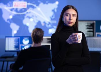 Mujer mirando a la cámara con un fondo de una persona trabajando en un computador y un diseño de continentes arriba de él
