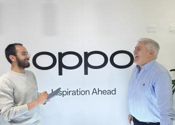 Fotografía de dos personas hablando con un letrero de fondo que dice Oppo