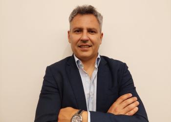 Foto de una persona posando frente a la cámara, cuenta con camiseta, blazer negro, reloj y pelo blanco