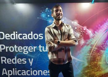 Foto de una persona cruzada de brazos con un fondo que dice dedicados a proteger tus redes y aplicaciones