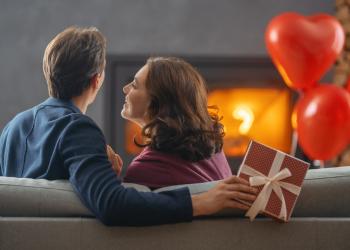 Foto de un hombre y una mujer sentados en un sofa mirando a la chimenea, están abrazados