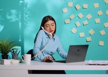 Mujer hablando por teléfono, mirando el computador y con muchos stickers pegados en la pared