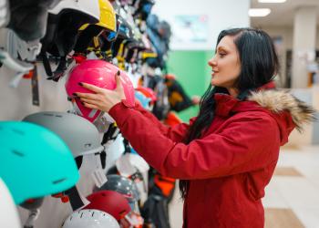 Una mujer con chaqueta roja toma un casco rosado de un local