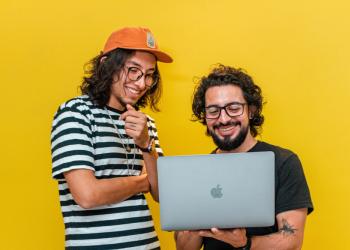 foto de dos personas mirando un pc con fondo amarillo