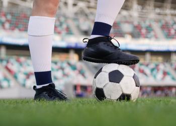 Foto de una persosona con guaybos y un balón de fútbol sobre su pie derecho