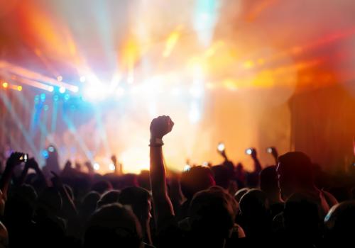 Foto de una multitud con una persona levantando el puño por encima de los demás, fondo multicolor de luces del escenario