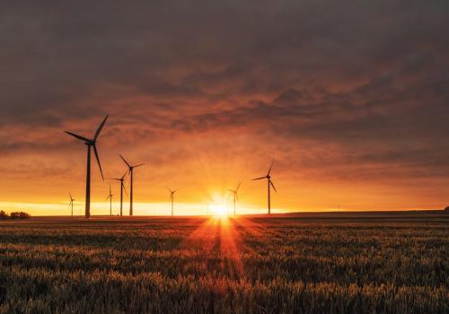 Día de la energia, foto de una puesta de sol con una imagen de energia eólica de fondo