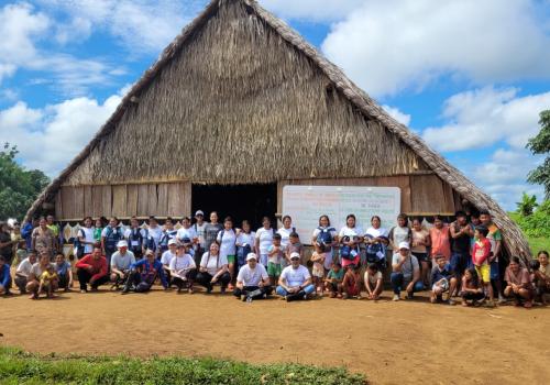 Foto de una casa en paja con 30 personas al frente de ella posando para una fotografía