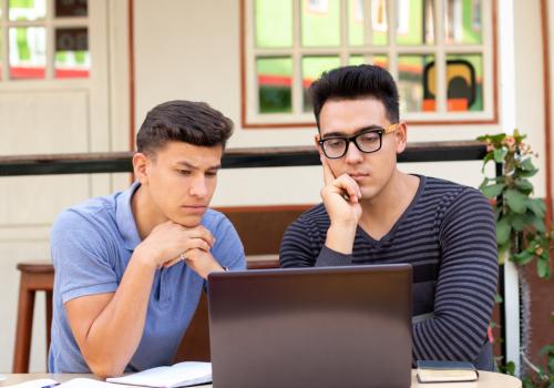 Foto de dos jóvenes mirando el computador mientras piensan