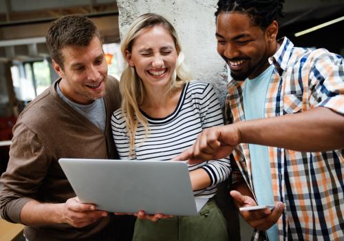 Foto de tres personas mirando un computador y sonriendo a la cámara