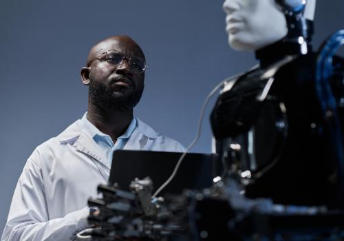 Foto de un hombre americano escribiendo sobre un teclado y mirando un robot