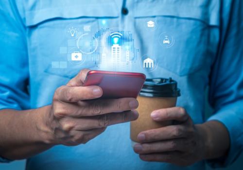 Foto de un hombre utilizando su celular en una mano y con un café en la otra