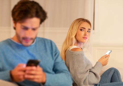 Foto de una mujer con un celular en la mano mirando de forma sospechosa a su pareja que habla por celular