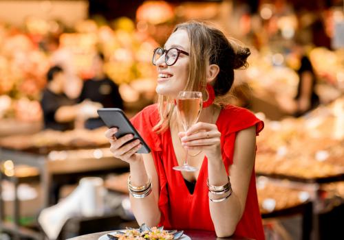 Foto de una mujer con un celular en la mano y una copa en la otra