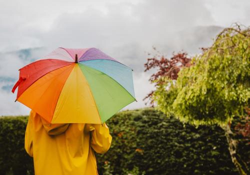 Foto de una mujer con un paraguas abierto de varios colores  de fondo a la cámara