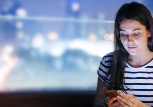 Foto de una mujer mirando el celualr y de fondo una ciudad difuminada