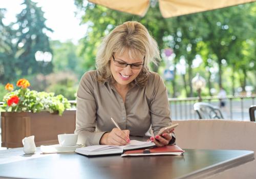 Foto de una mujer rubia anotando algo en un cuaderno con un fondo de arboles